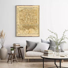 a living room with a large wall-mounted map of a city, a gray sofa with striped pillows, a wooden side table, and a round coffee table with books and a vase of greenery.