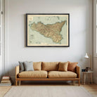 a large framed map of Sicily hanging on a wall above a brown sofa with pillows.