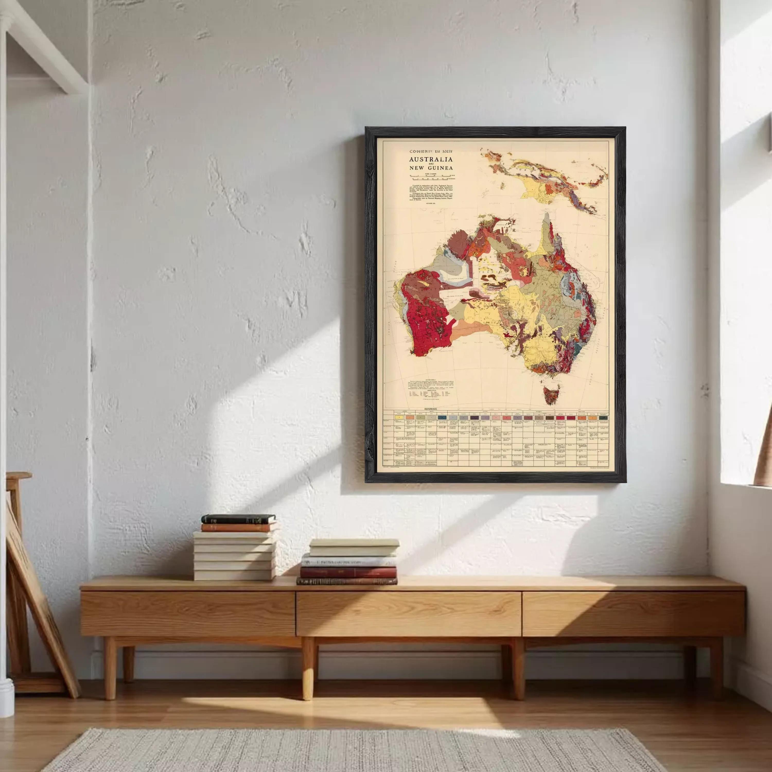 a framed map of Australia hanging on a wall, with a stack of books and a wooden bench below it.