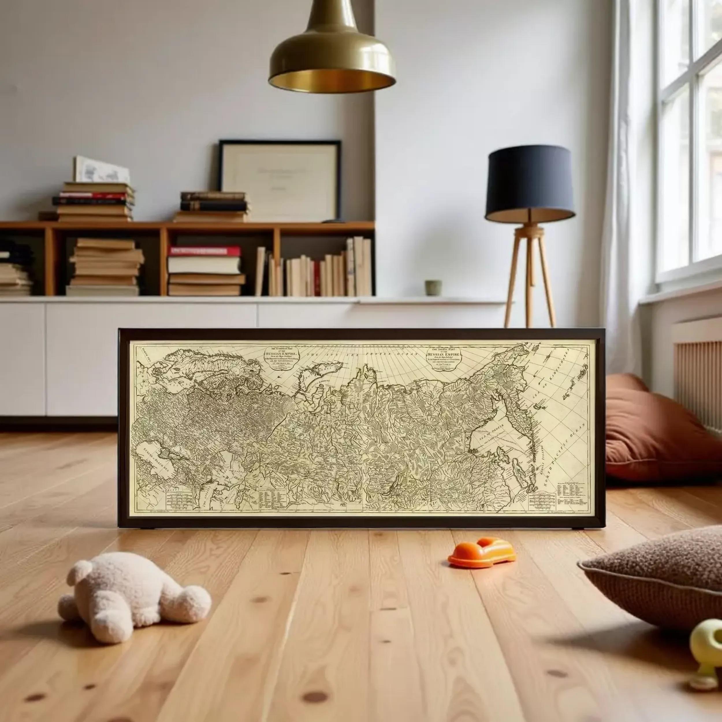 a large framed map of the world on a wooden floor, with a lamp and some books in the background.