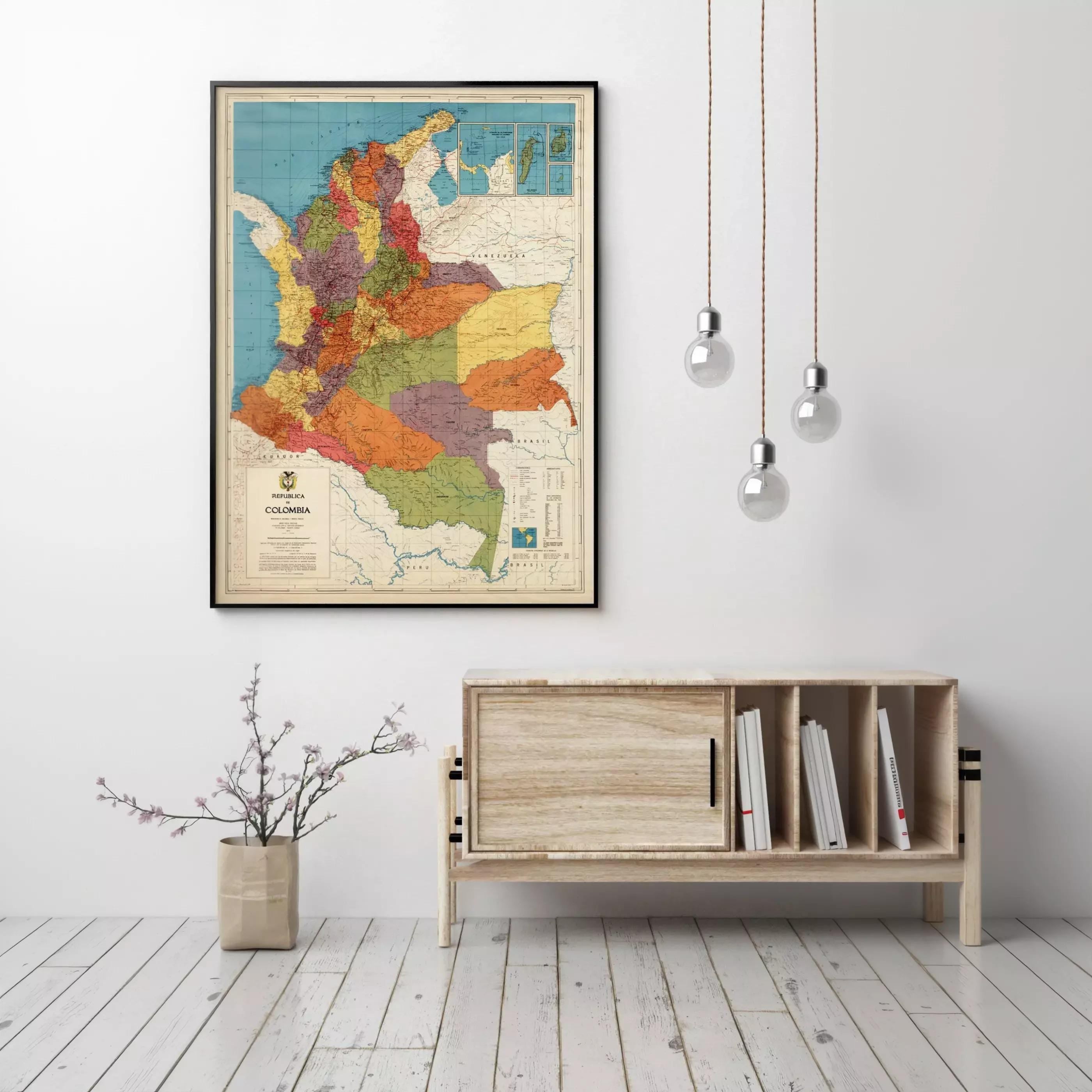 a framed map of Colombia hanging on a wall, with a wooden cabinet below it and a vase of flowers on the floor.
