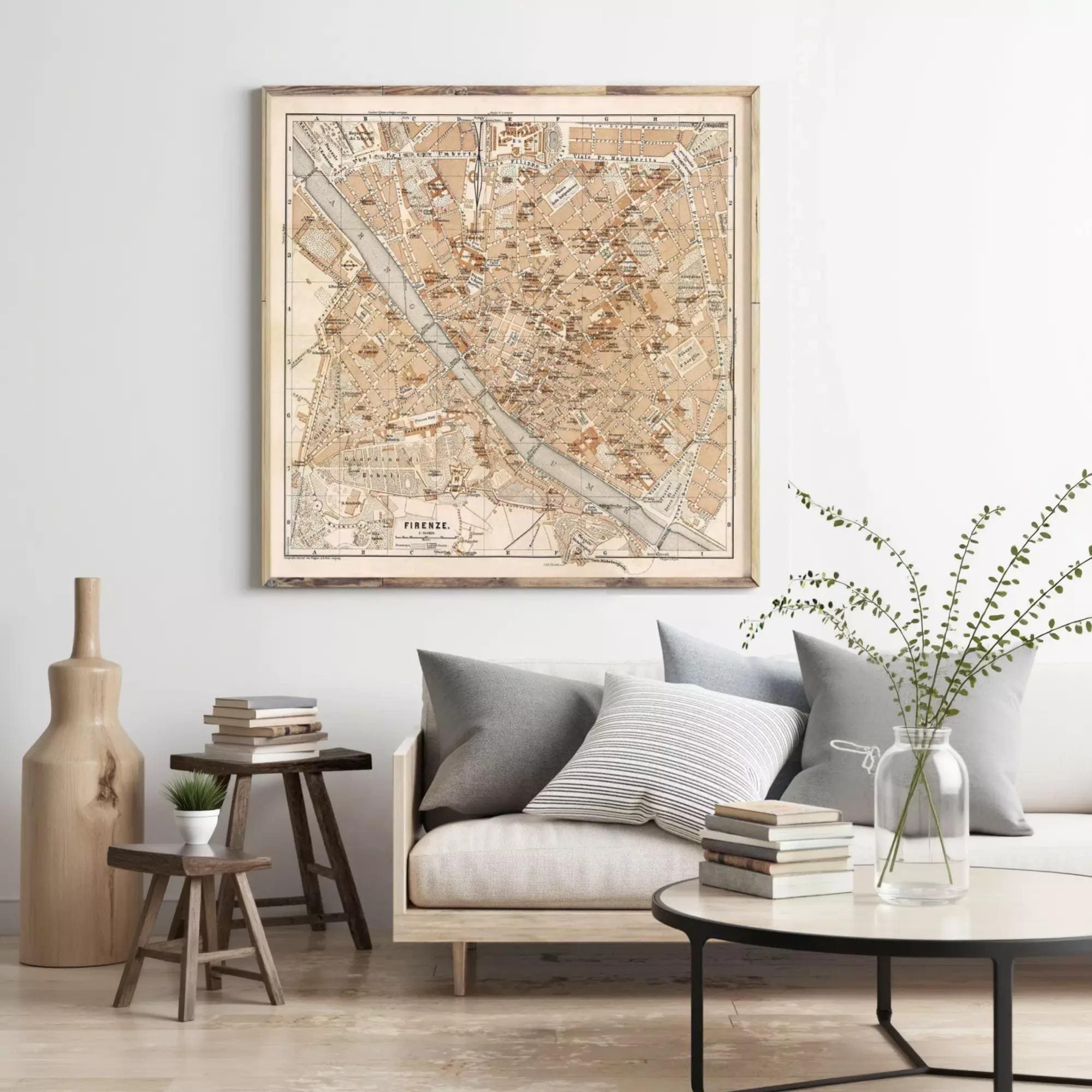 a living room with a large framed map of Florence, Italy, hanging on the wall above a couch with pillows. The room also includes a coffee table with books and a vase with greenery.