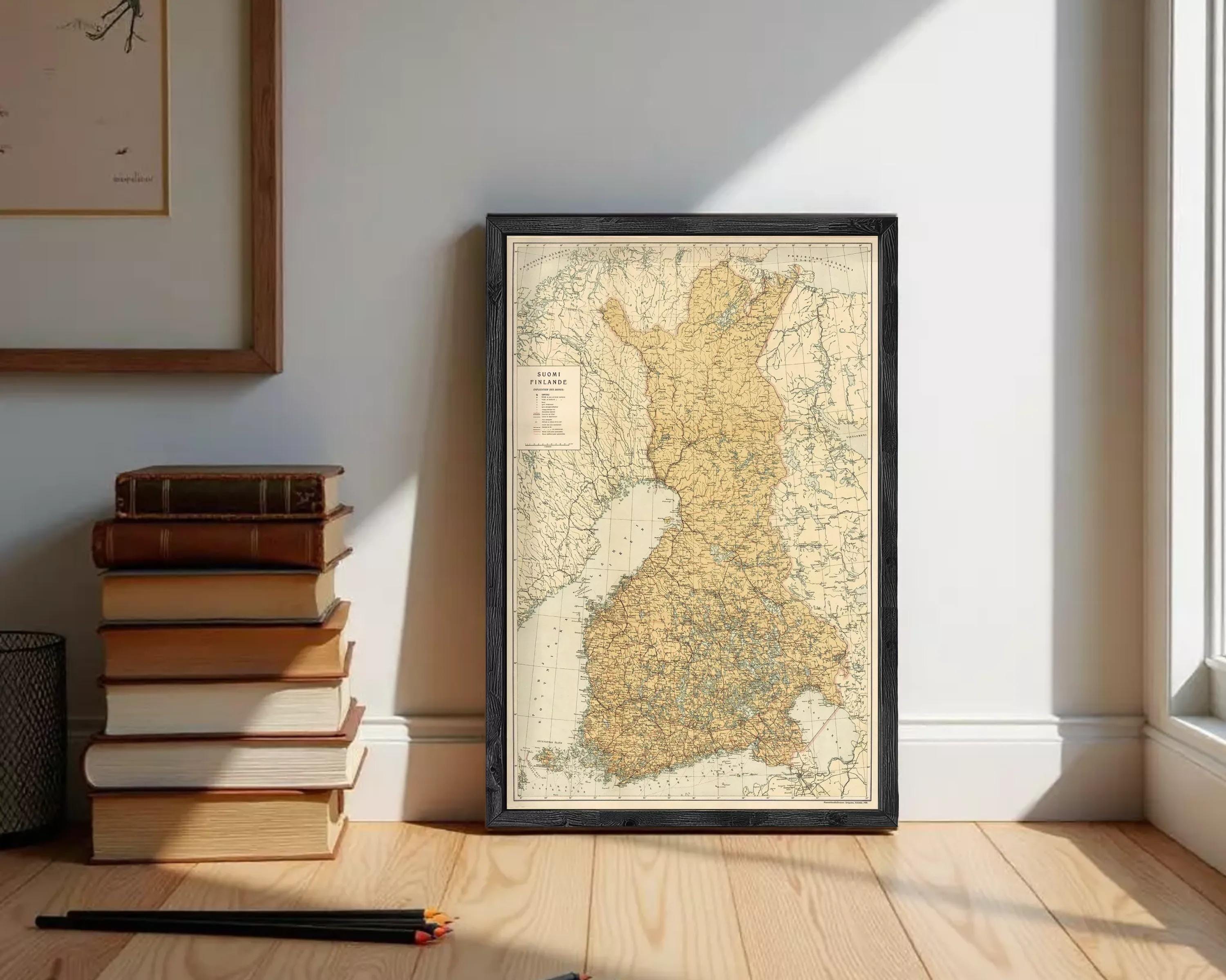a framed map of Finland, with a stack of books and a pile of pencils on the floor in front of it.