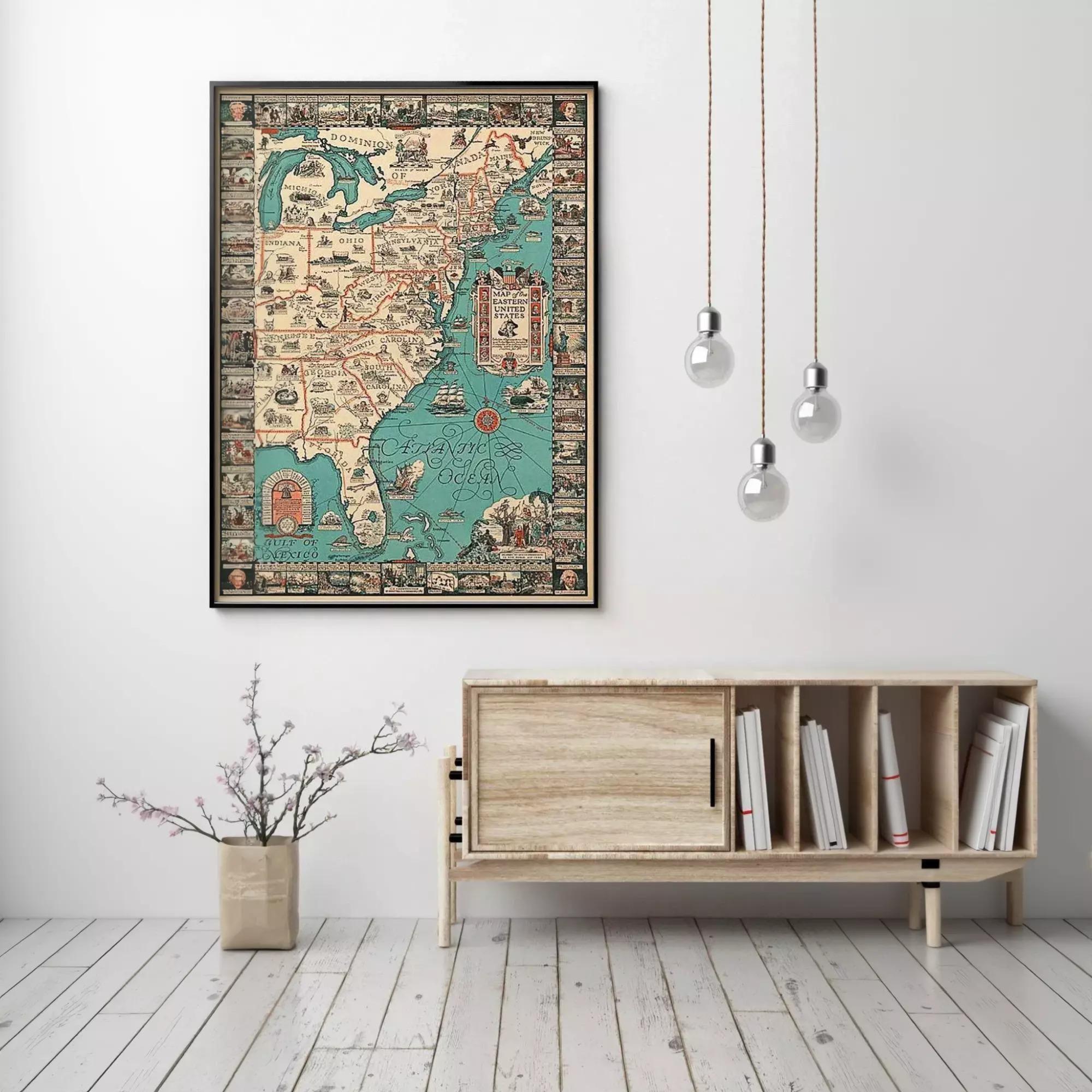 a large framed map of the United States hanging on a white wall, with a wooden cabinet below it and a vase of flowers on the floor.