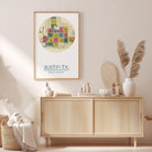 a framed map of Austin, Texas, hanging on a wall above a wooden cabinet. The cabinet has various items on it, including a vase with pampas grass, a bottle, and a bowl.