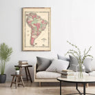 a living room with a large framed map of South America hanging on the wall above a couch with pillows. There are also some books and a vase with flowers on the couch, creating a cozy and inviting atmosphere.