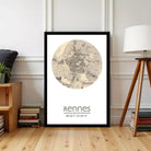 A framed map of Rennes, a city in France, is displayed on a wall in a room with a wooden floor and a lamp.