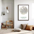 a minimalist living room with a wooden chair, a pendant light, a framed map of Florence, and a stack of books.