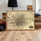 A framed map of a city, likely Paris, displayed on a wooden floor in front of a stack of books.