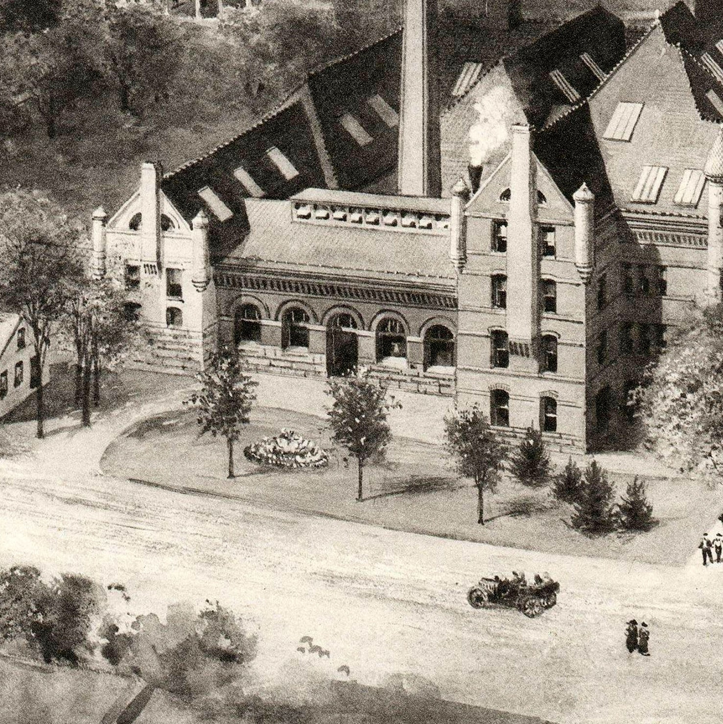 A black and white image depicting a large, multi-story brick building with a prominent chimney, surrounded by trees and a paved road.