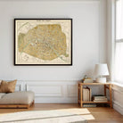 a large framed map of Paris hanging on a white wall, with a wooden side table and a lamp next to it.
