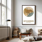 a cozy living room with a large framed map of Santa Barbara, California, hanging on the wall. The room has a comfortable seating area with a wooden chair and a stack of books, as well as a lamp and a window providing natural light.