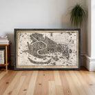 A framed map of Venice, Italy, depicting the city's layout and surrounding areas, is displayed on a wooden floor in a room.