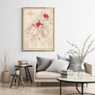 a living room with a framed map of a city hanging on the wall, a wooden coffee table with books and a vase of greenery, and a comfortable couch with pillows.