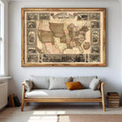 a large framed map of the United States hanging on a wall above a gray sofa with a wooden frame.