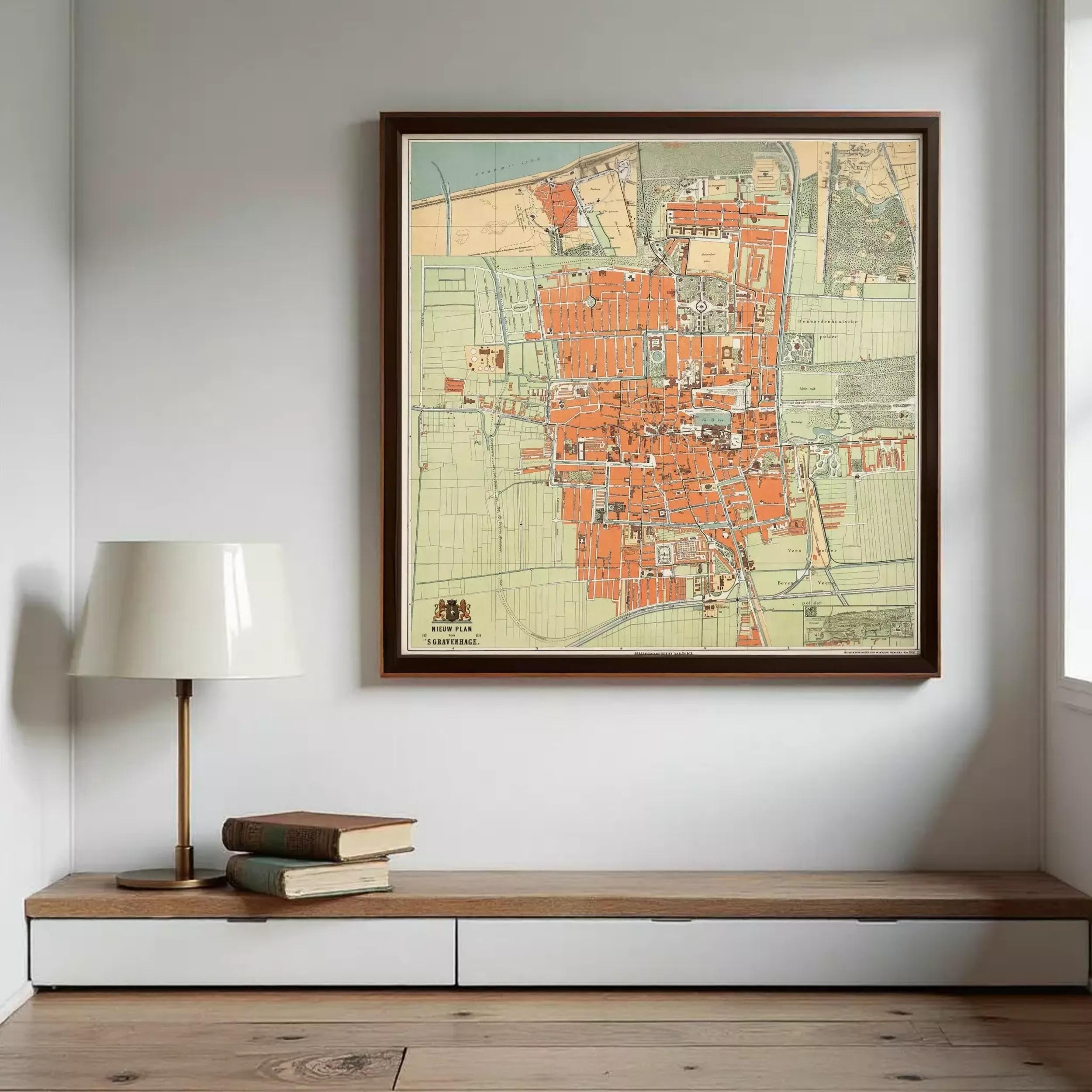 a large framed map of a city hanging on a wall, with a lamp and a stack of books placed below it.