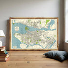 a large framed map of Vancouver, Canada, with a wooden floor and a stack of books nearby.