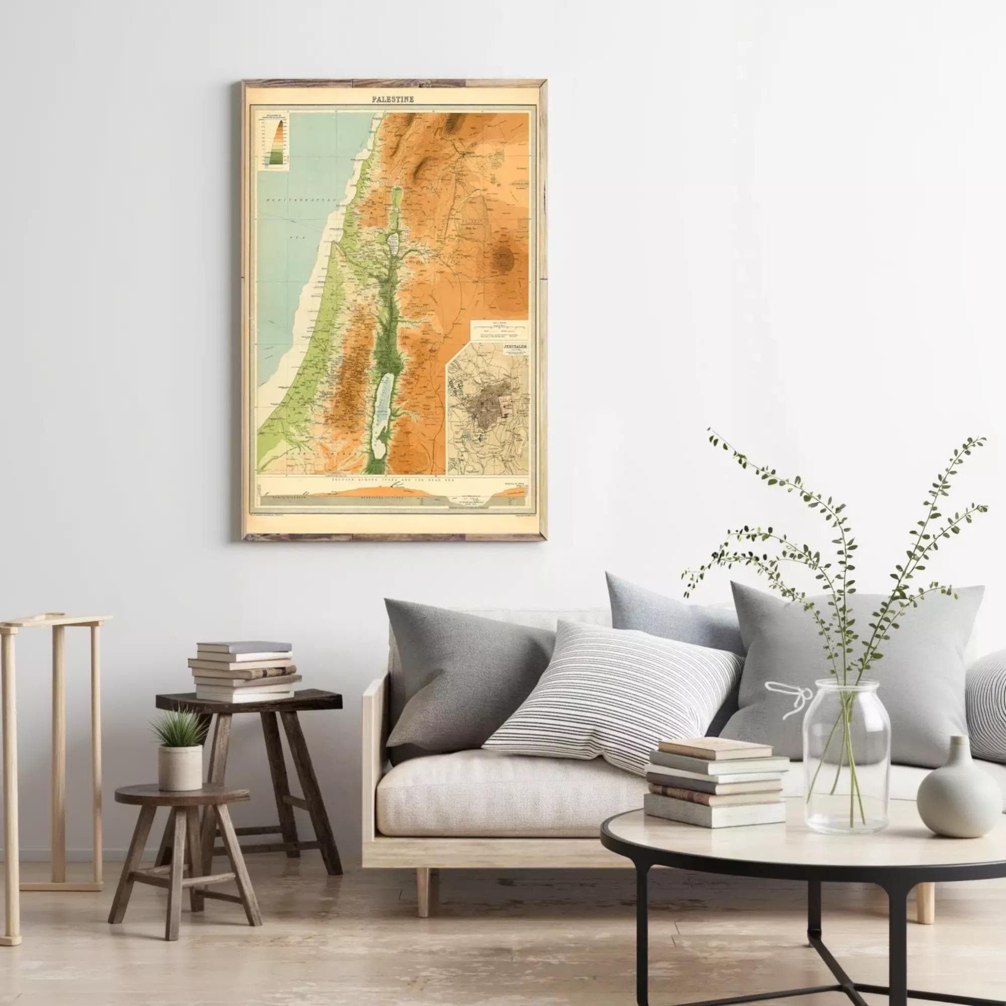 a living room with a framed map of the Middle East hanging on the wall, a wooden stool, a round coffee table with books and a plant, and a gray couch with pillows.