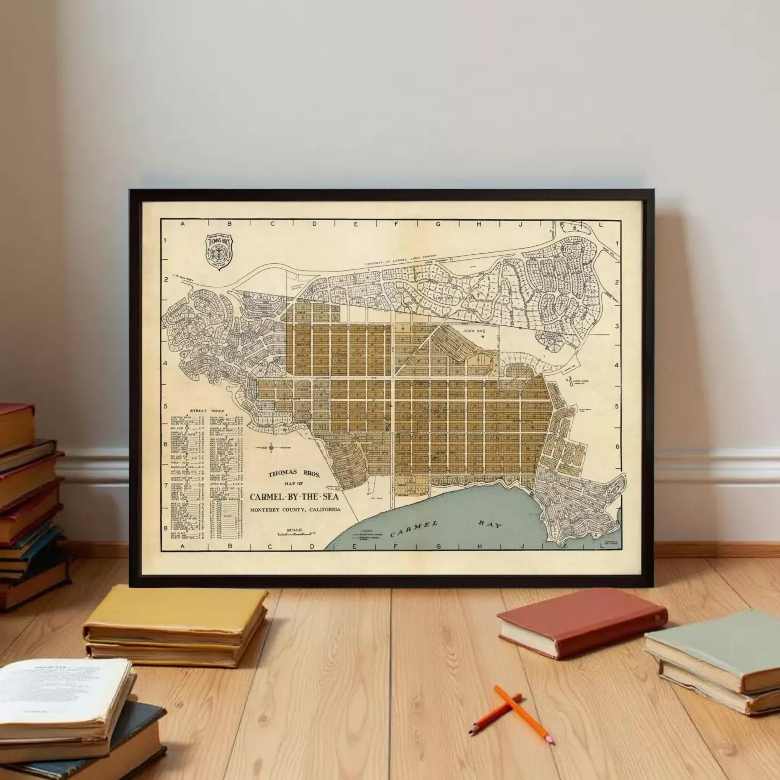 a framed map of Carmel by the Sea, with a stack of books and a few pencils on the floor in front of it.