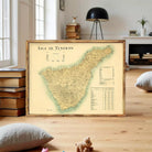 A framed map of the Canary Islands, specifically Isla de Tenerife, is displayed in a living room setting with books and a lamp in the background.
