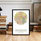 A framed map of Providence, Rhode Island, with the city's name and location printed on it, placed on a wooden floor in front of a stack of books.