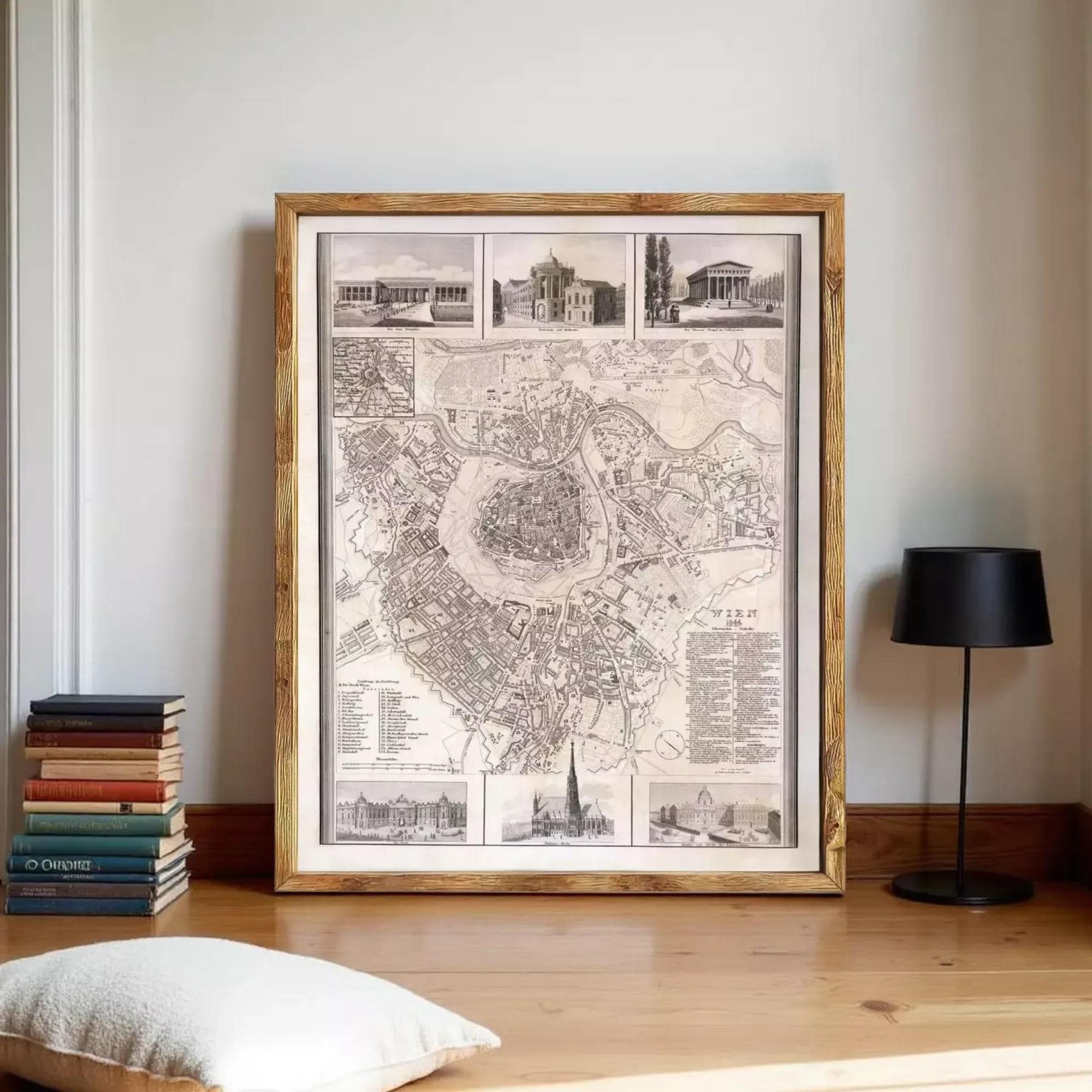 a large framed map of a city, with various buildings and landmarks depicted on it. The map is displayed on a wooden floor, with a stack of books and a lamp to the side.