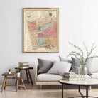 a living room with a large framed map hanging on the wall above a couch with pillows. There are also some books and a vase with flowers on the couch, creating a cozy and inviting atmosphere.
