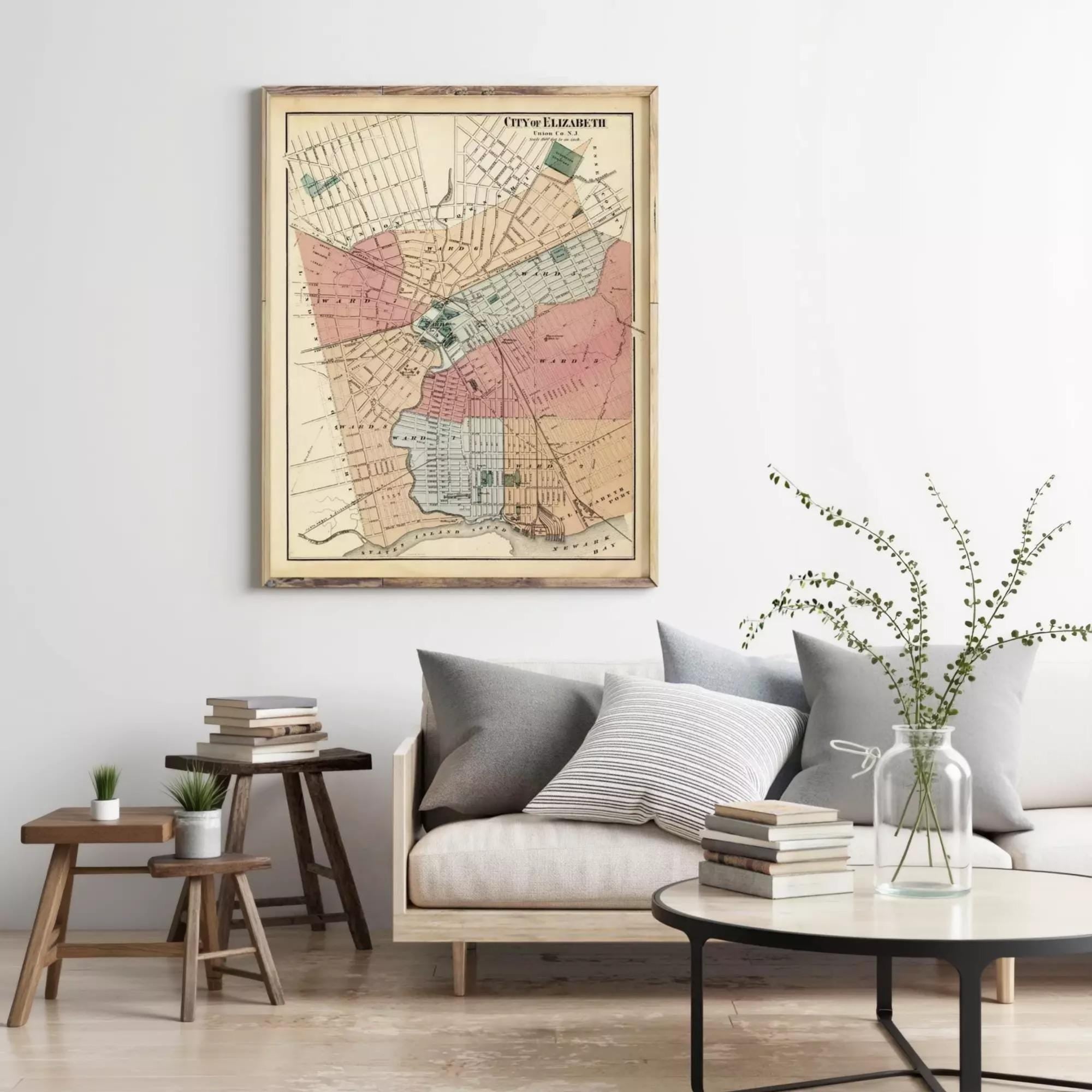 a living room with a large framed map hanging on the wall above a couch with pillows. There are also some books and a vase with flowers on the couch, creating a cozy and inviting atmosphere.