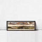 A framed painting depicting a cityscape with a cloudy sky in the background.