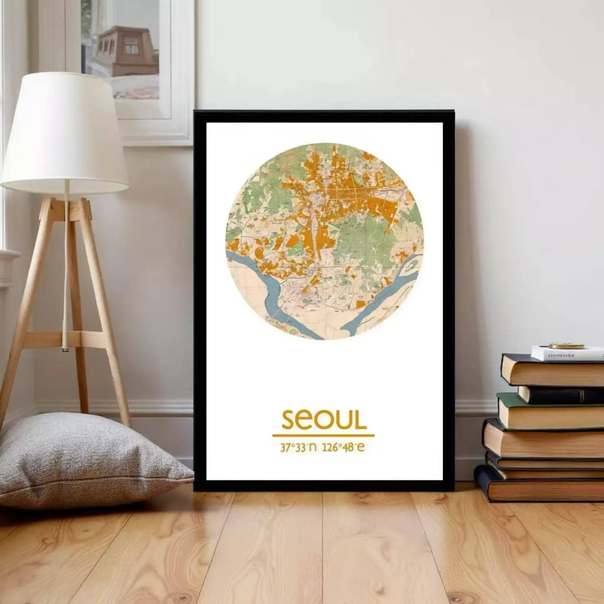 A framed map of Seoul, South Korea, with the city's location and surrounding areas marked on it. The map is displayed on a wooden floor, with a stack of books and a lamp nearby.