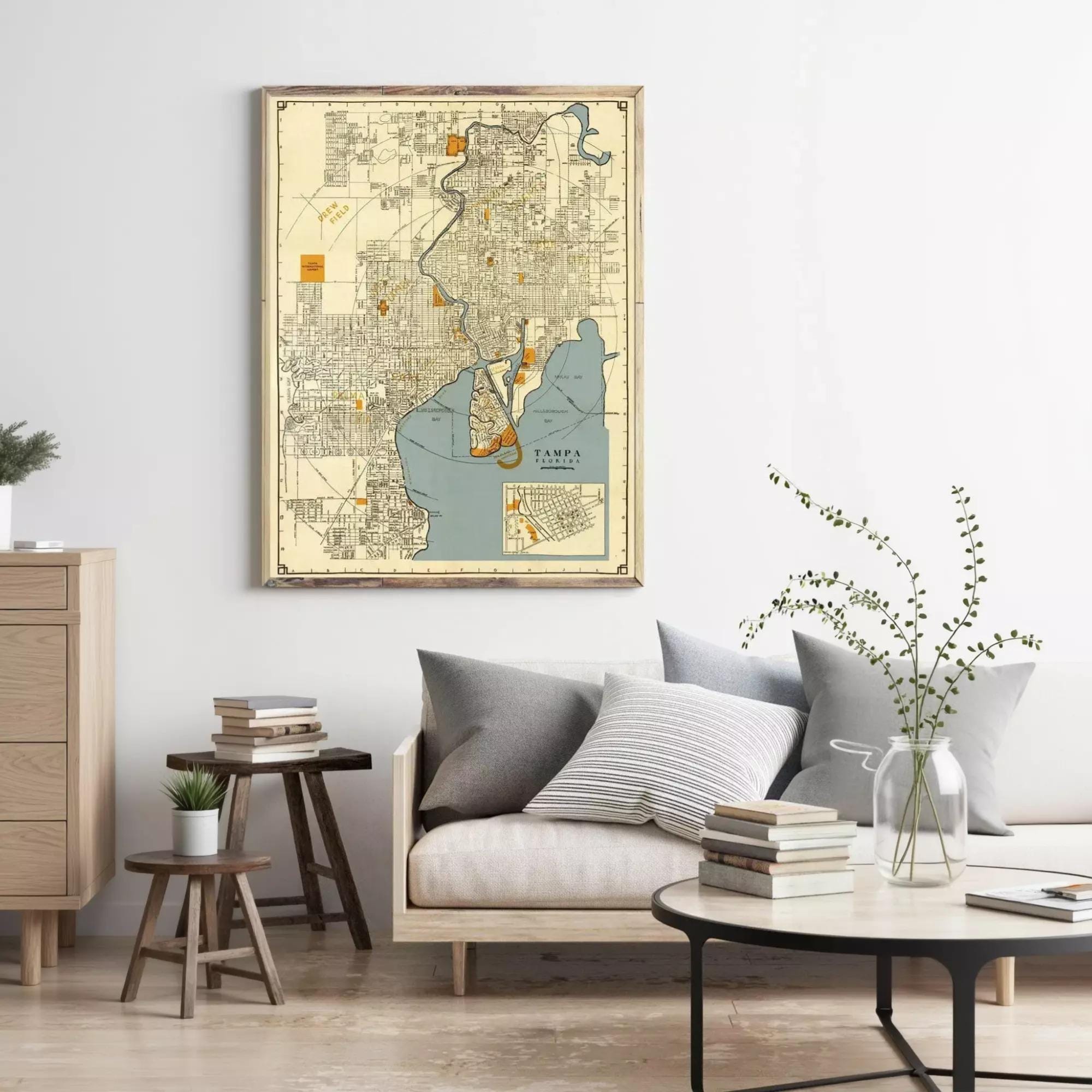 a living room with a large framed map of San Francisco hanging on the wall above a couch with pillows. The room has a wooden coffee table, a side table with books, and a potted plant.