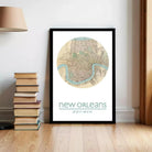 A framed map of New Orleans, with a river and surrounding area, is displayed on a wall next to a stack of books.