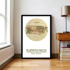 A framed map of Puerto Rico is displayed on a wall in a room with a lamp and bookshelf.