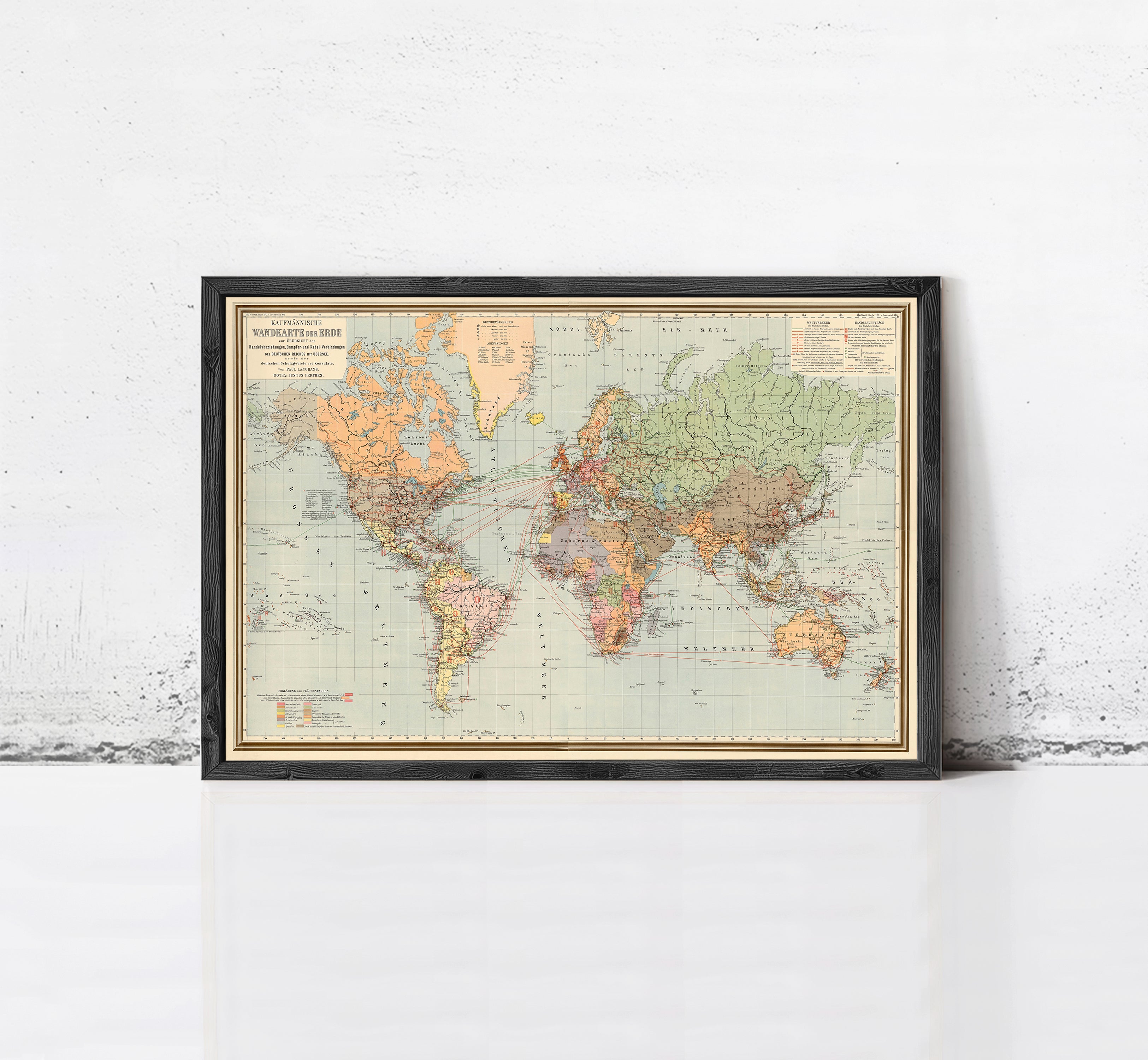 The image is a framed vintage world map with a black border and gold trim, displayed on a white wall.
