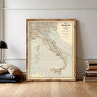 A framed vintage map of Italy is displayed on a wall, surrounded by a stack of books and a lamp.