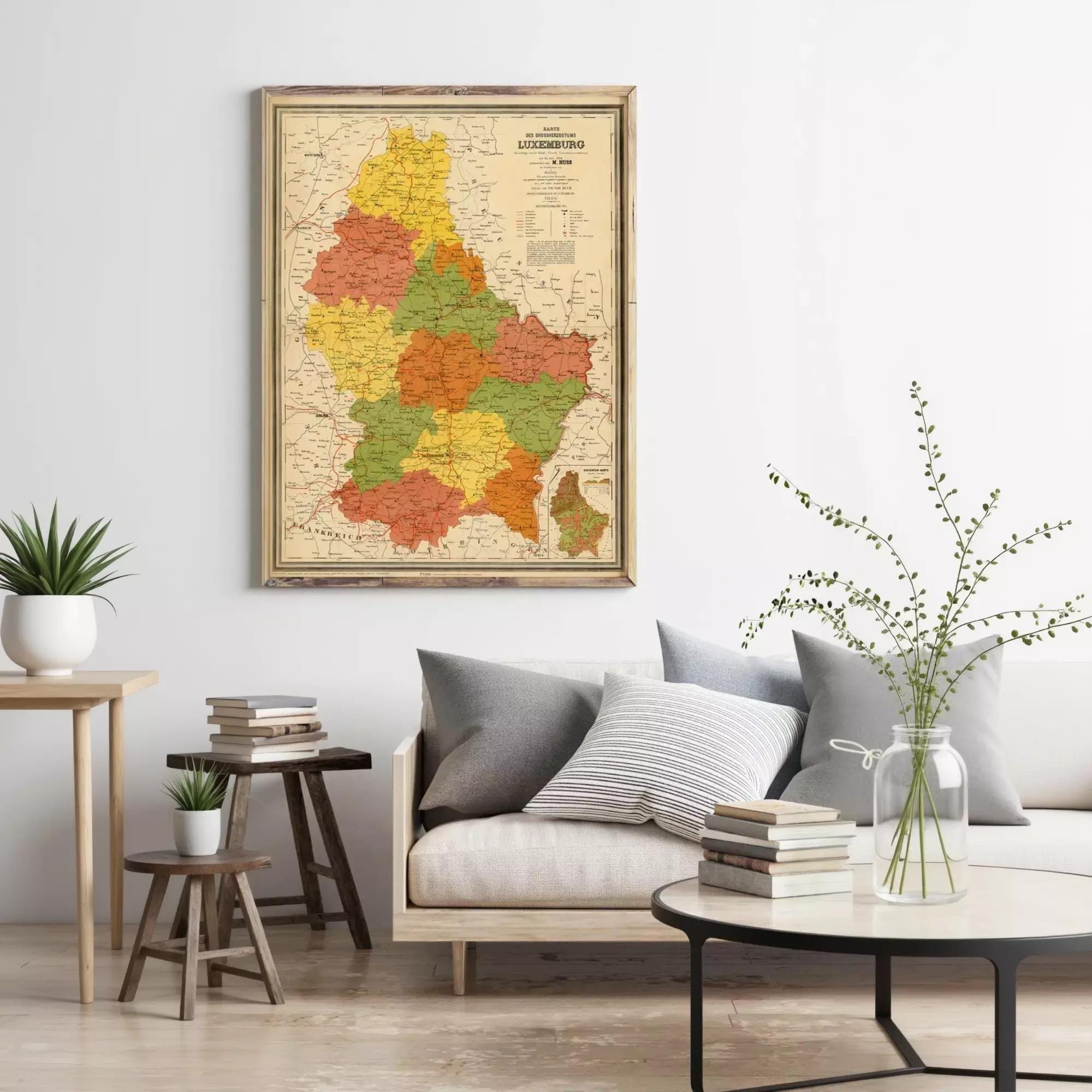 a living room with a large framed map of a region hanging on the wall, a couch with pillows, a coffee table with books and a vase of flowers, and a small table with a plant.