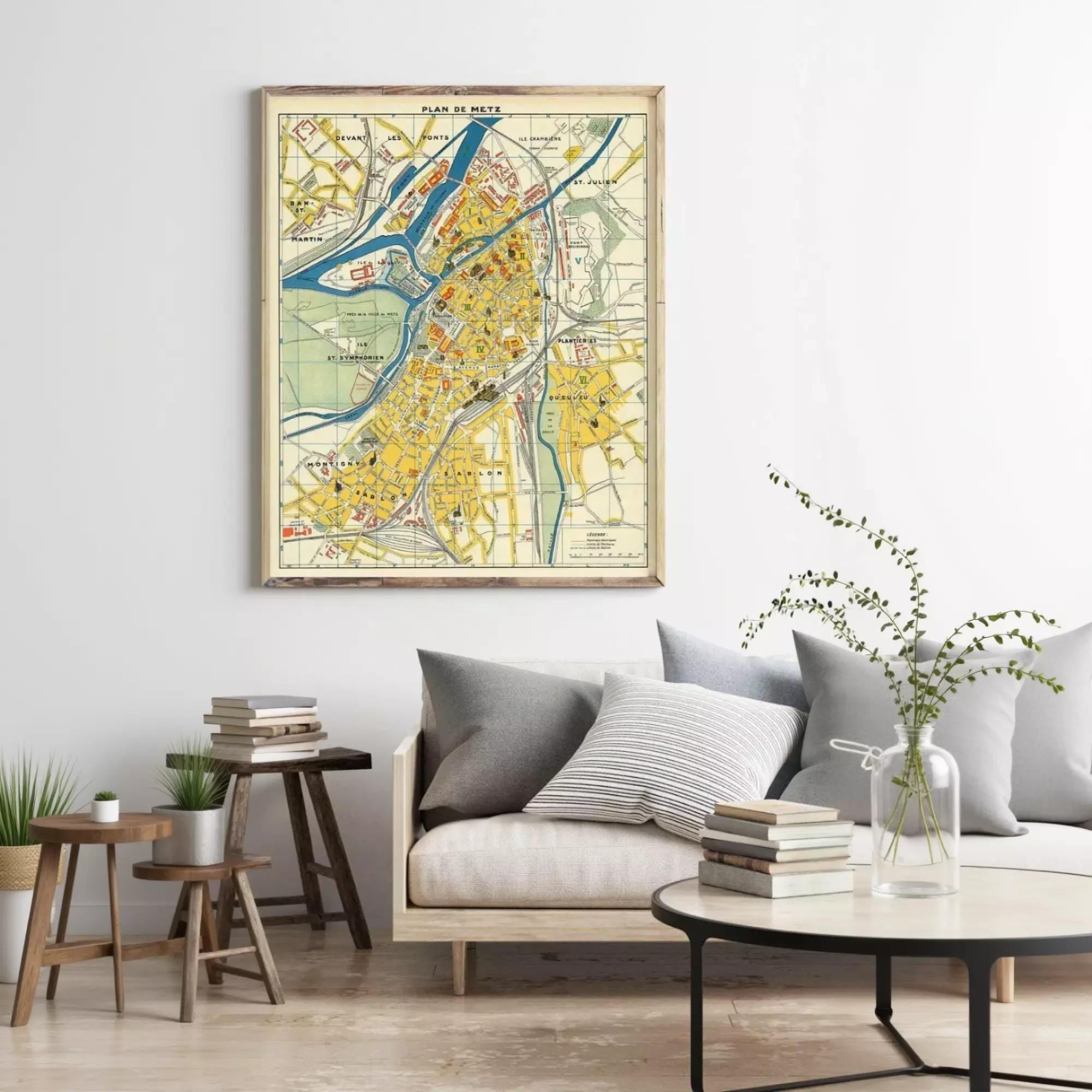 a living room with a large framed map of a city hanging on the wall above a couch with pillows. The room also includes a coffee table with books and a vase with greenery.