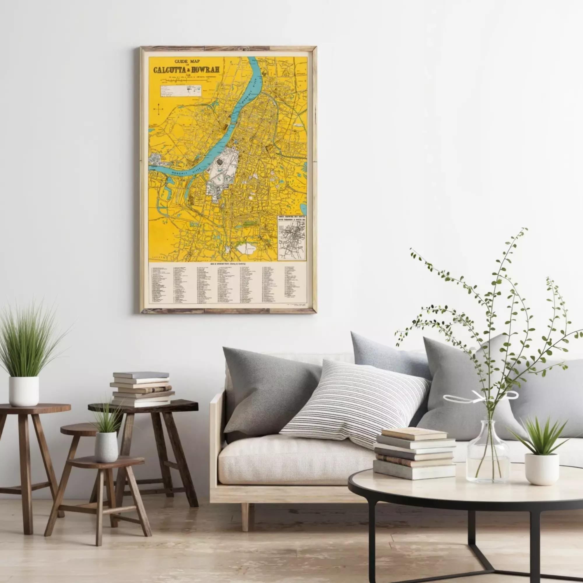 a living room with a large yellow map of Calcutta, India, hanging on the wall above a gray sofa. The room is decorated with potted plants, books, and a round coffee table.
