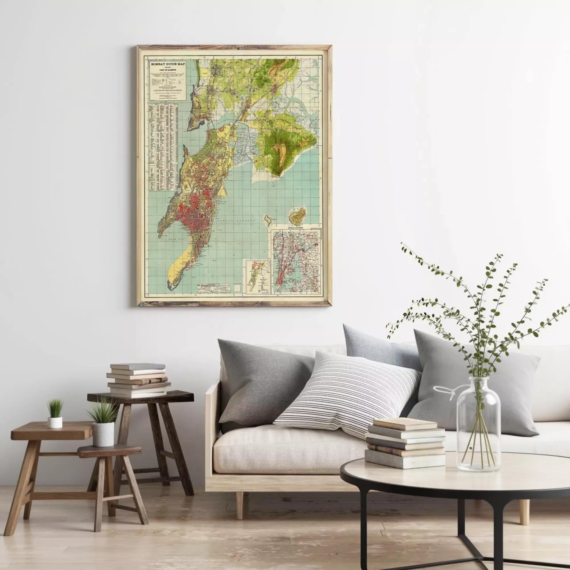 a living room with a large framed map hanging on the wall above a couch with pillows. There are also two small tables with books and plants on them, and a round coffee table in front of the couch.