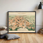 The image is a framed vintage map of a city, depicting a detailed and colorful cityscape with various buildings, roads, and natural elements.