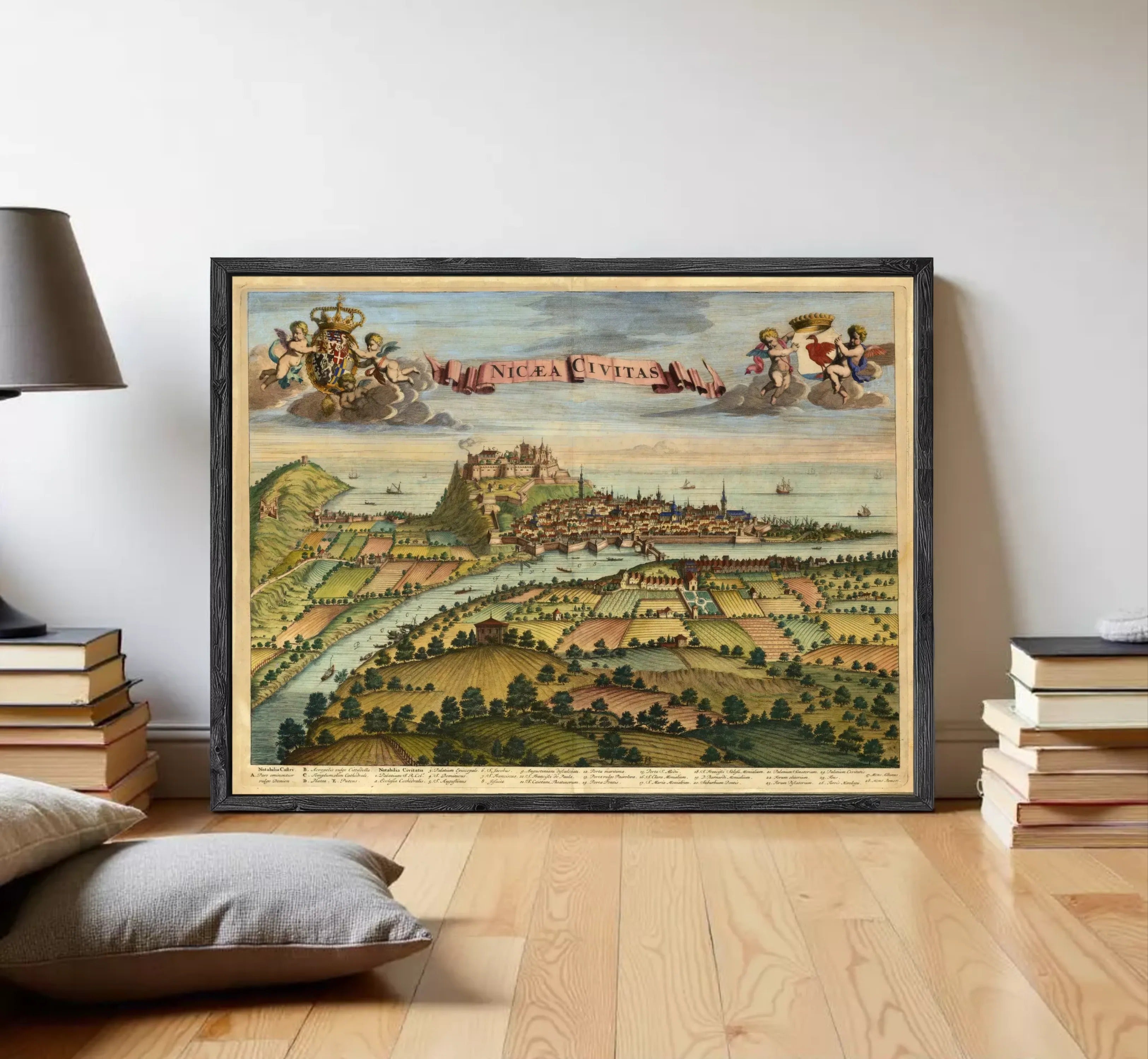 The image is a framed vintage map of a city, depicting a landscape with a river, buildings, and people.