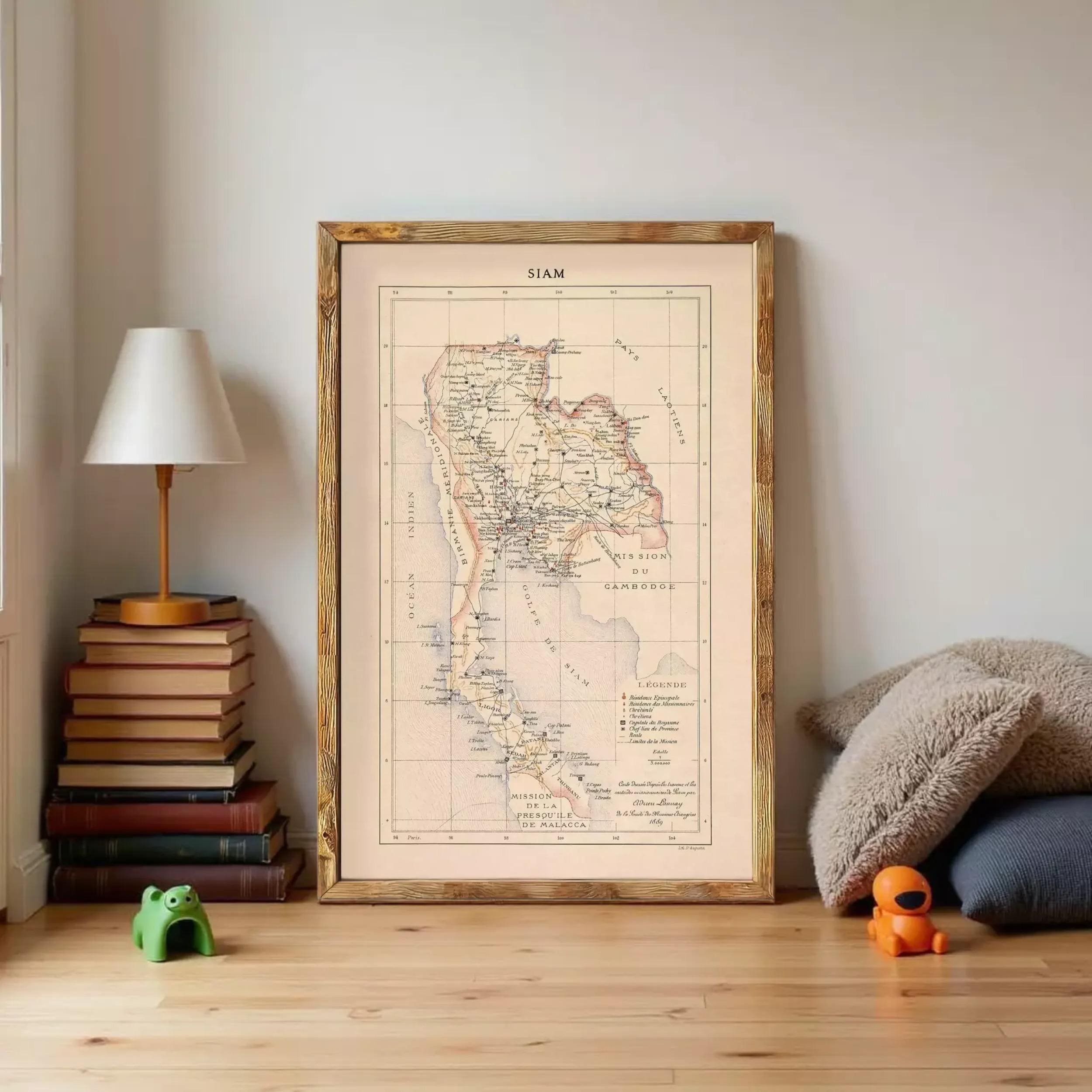 a framed map of Thailand, with a lamp, books, and stuffed animals on a wooden floor in the background.