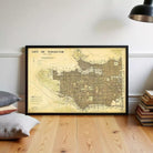 a framed map of Vancouver, Canada, with a wooden floor and a stack of books in the background.
