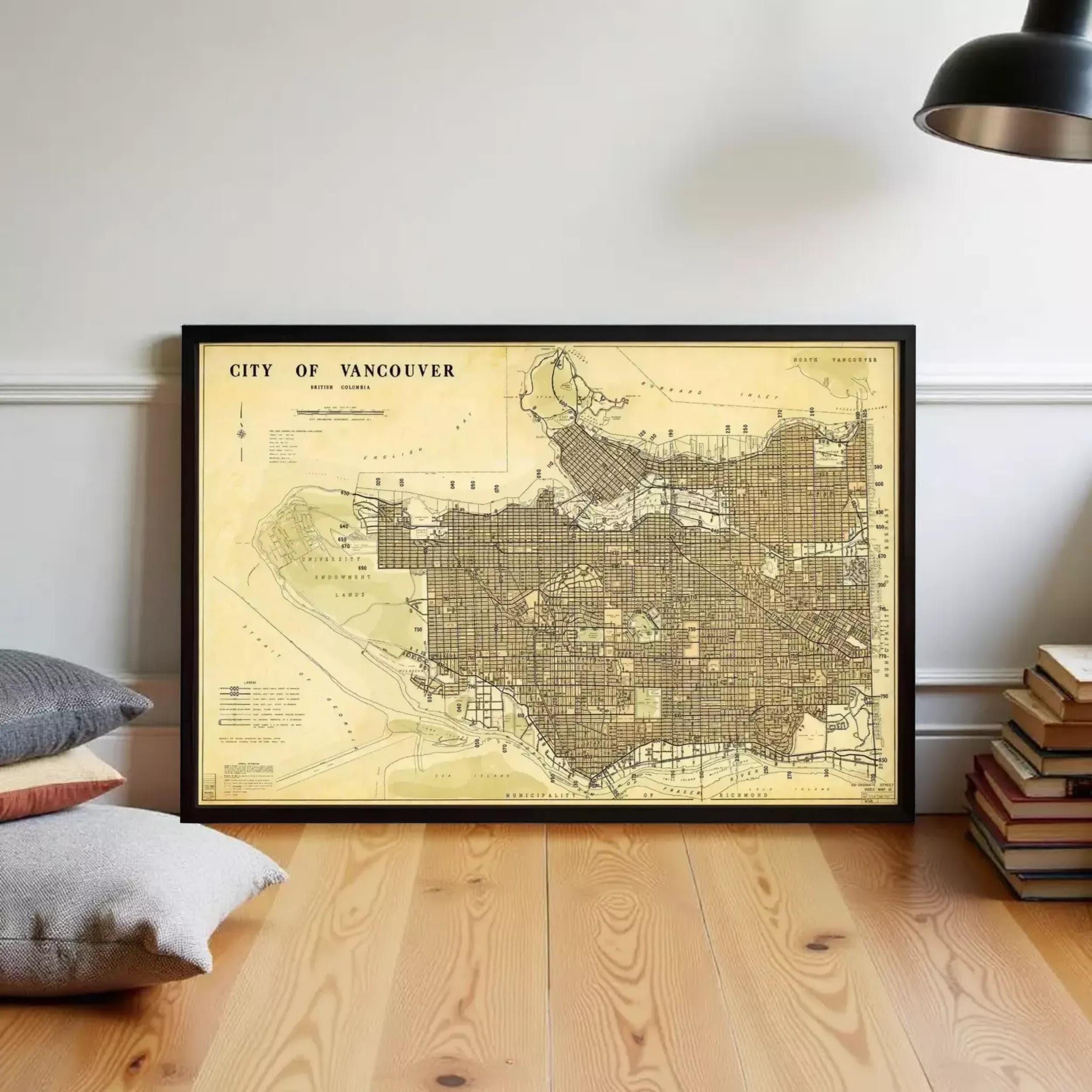 a framed map of Vancouver, Canada, with a wooden floor and a stack of books in the background.