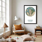 a cozy living room with a large framed map of Sydney, Australia, hanging on the wall. The room is furnished with a chair, a lamp, and a bookshelf filled with books. There are also some toys scattered around the room, adding a playful touch to the space.