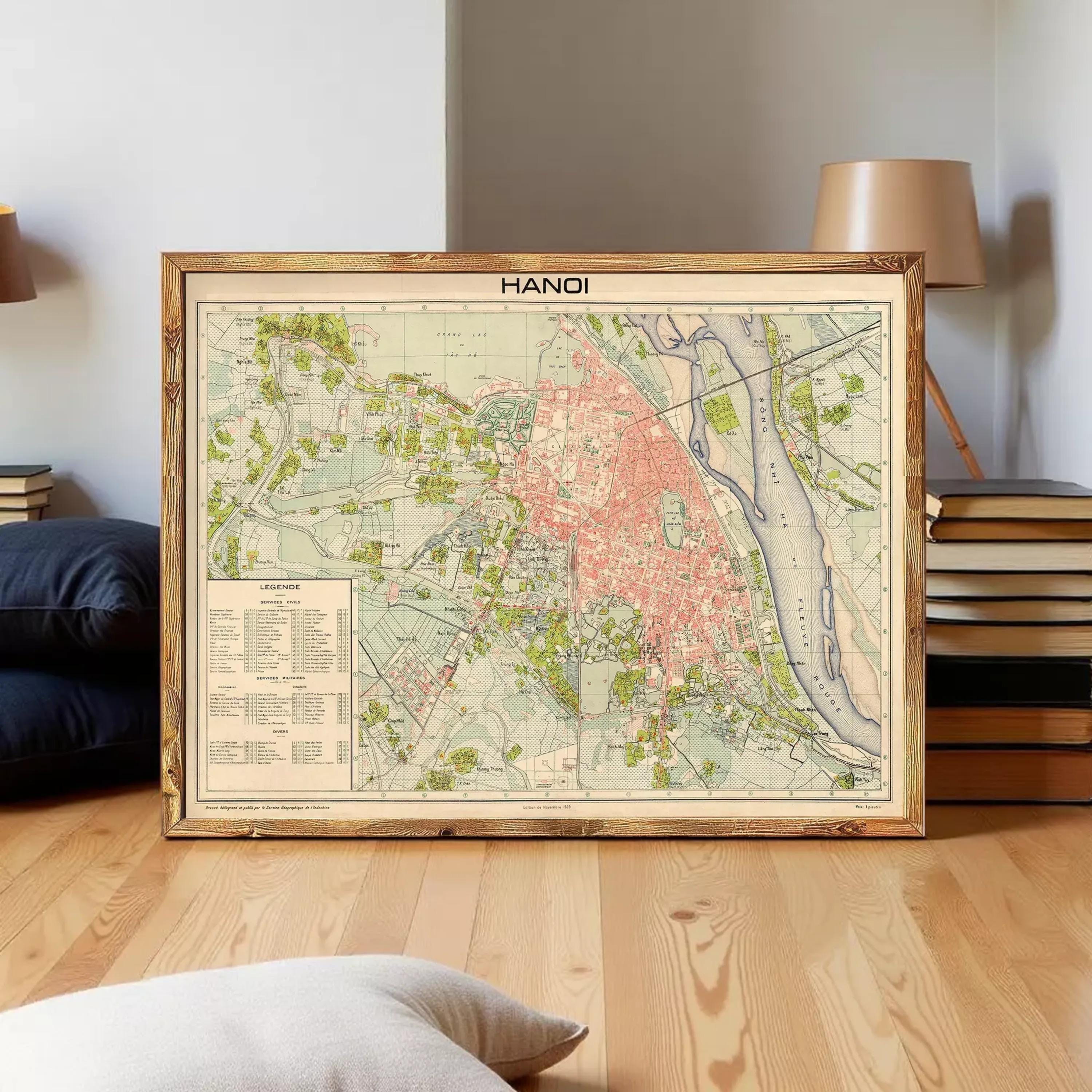 a framed map of Hanoi, Vietnam, displayed on a wooden floor in a room with a lamp and books in the background.