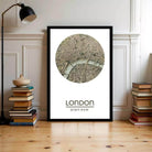 A framed map of London with a circular design on the front, placed on a wooden floor next to a stack of books.