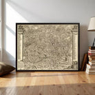 A large framed map of a city or region, with intricate details and labels, displayed on a wooden floor in a room with books and a lamp.