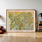 The image is a large framed map of Los Angeles, California, with various landmarks and cityscapes depicted in a colorful and detailed manner.