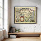 a framed map of Africa hanging on a wall, with a wooden shelf below it holding several books and a potted plant.